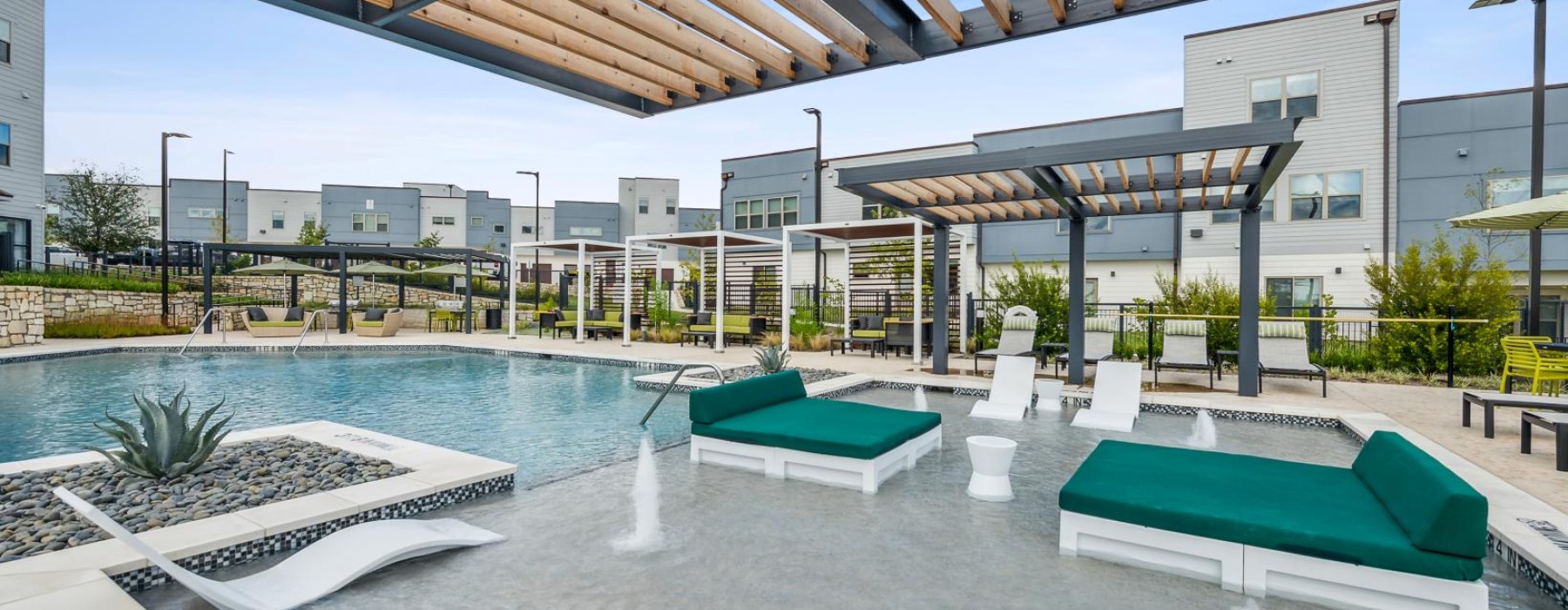 a pool with lounge chairs and a covered area with a building in the background